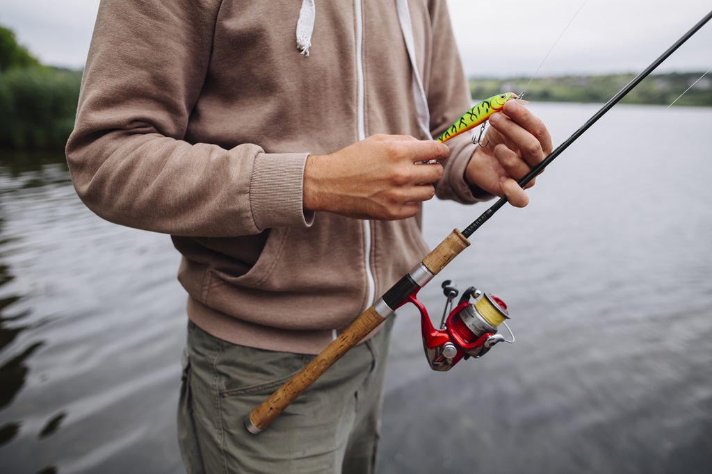 Um homem em um lago segura  uma vara de pesca.